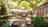 tables impeccablement mises sur une terrasse ensoleillée, chaises de jardin en métal noir, parasols blancs et nappes blanches, vert en arrière-plan