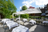 impeccably set tables on a sunny terrace, black metal garden chairs, white parasols and white tablecloths, greenery in the background