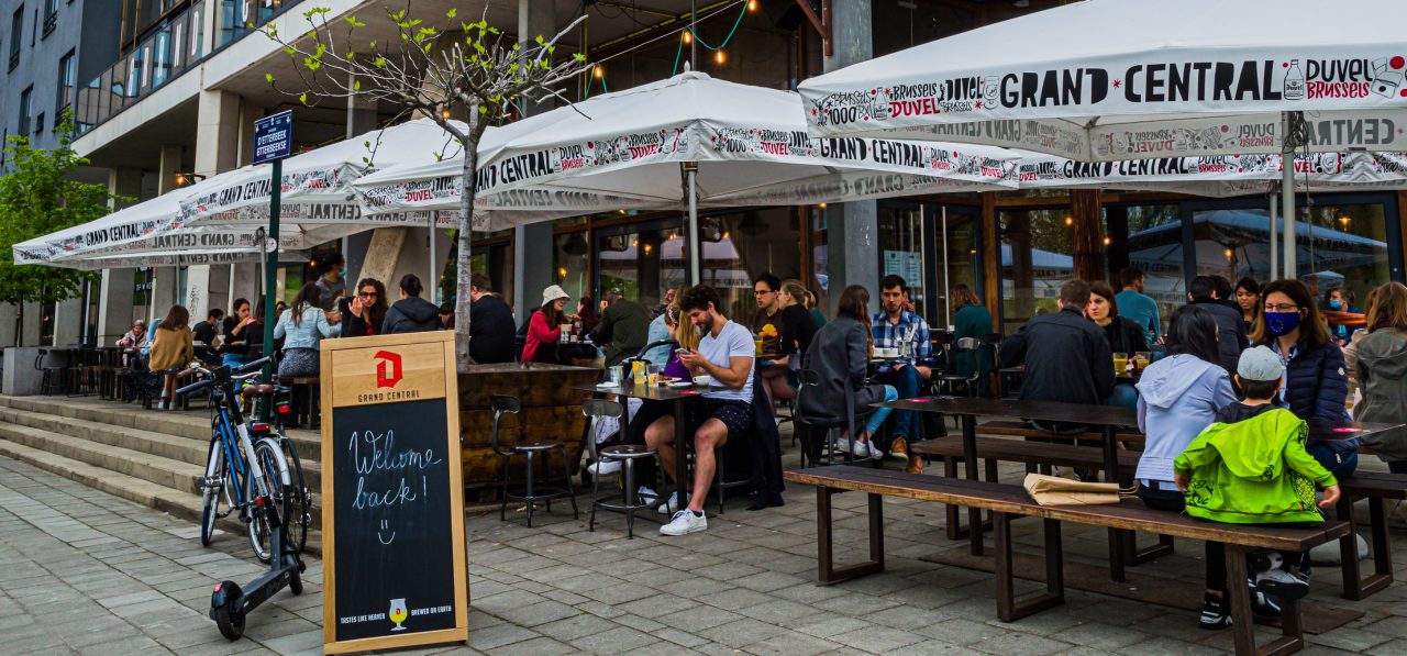 Die Terrasse am Grand Central: Menschen sitzen unter Sonnenschirmen und auf einem Duvel-Schild steht: welcome back!