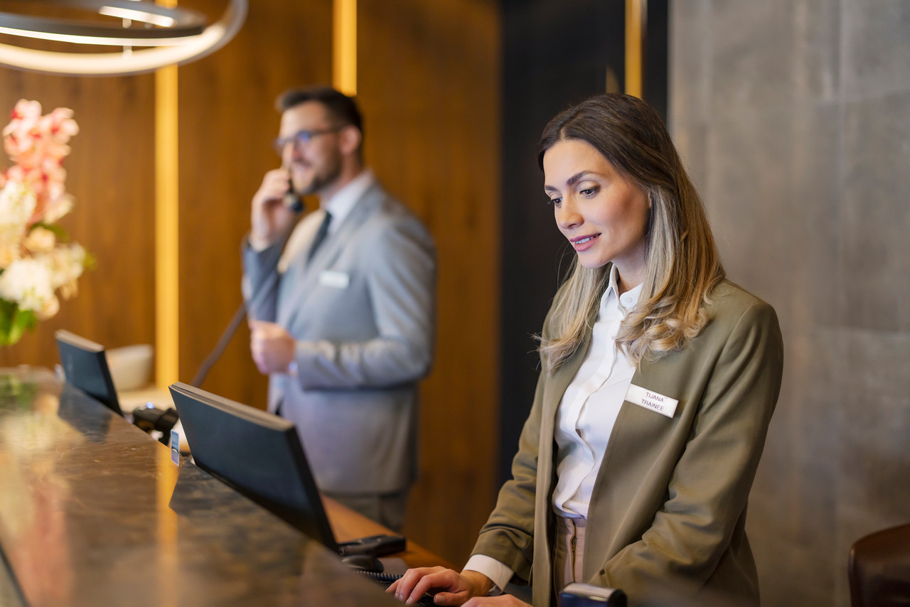 Attractive female receptionist working at hotel counter with her colleague in the background. Hotel concierge.