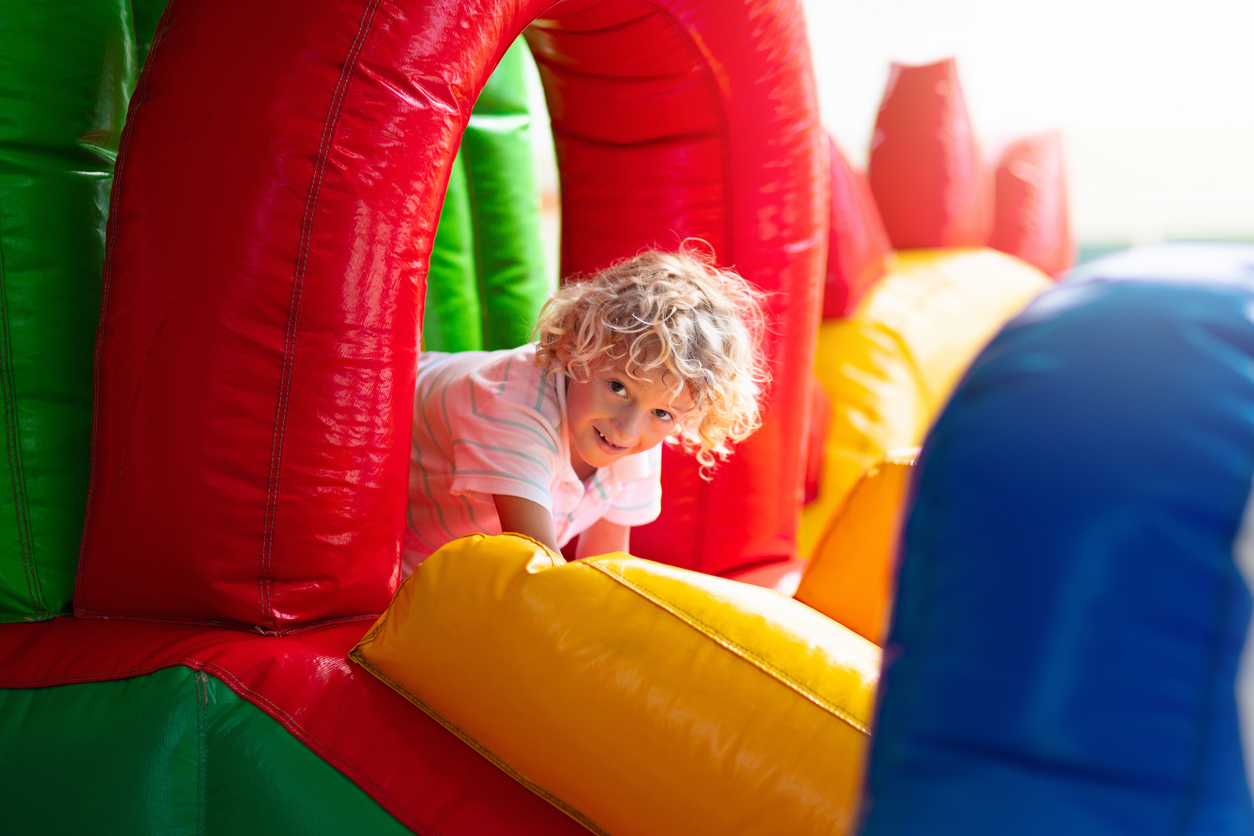 Child jumping on colorful playground trampoline. Kids jump in inflatable bounce castle on kindergarten birthday party Activity and play center for young child. Little boy playing outdoors in summer.